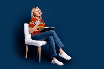 Wall Mural - Photo of glad cheerful nice woman wear stylish clothes sit chair hold book empty space isolated on dark blue color background