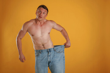 Wall Mural - Weight loss, shocked by results, big and huge pants or jeans. Man is against background in the studio