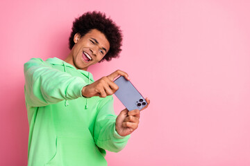 Canvas Print - Portrait of cool young man play game phone wear green hoodie isolated on pink color background