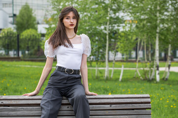 Wall Mural - Young woman sitting on a bench in a summer park