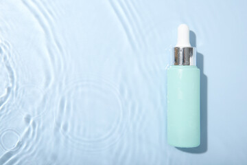 Sticker - Bottle of cosmetic product in water on light blue background, top view. Space for text