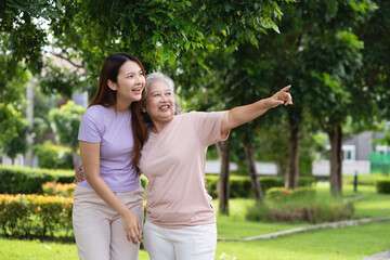 A woman and an older woman are standing in a park, pointing at something. The older woman is wearing a pink shirt and the younger woman is wearing a purple shirt. Scene is happy and friendly