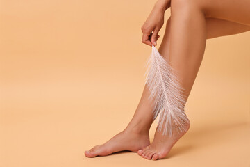 Poster - Woman with smooth legs and feather on beige background, closeup. Space for text