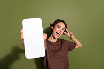 Poster - Photo portrait of pretty young girl hold telephone show v-sign excited dressed stylish brown outfit isolated on khaki color background