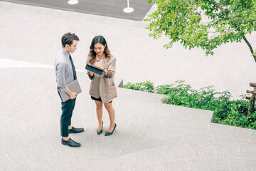 Two business professionals collaborate outdoors using a laptop and tablet to discuss work. emphasizes modern technology teamwork and communication. worker showcasing of technology in modern business.