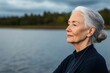© Lalida - A serene elderly woman gazes thoughtfully at the calm lake, embodying peace and reflection in a natural setting.