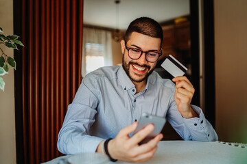 Wall Mural - Young caucasian man shopping online on mobile phone using credit card