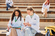 © Seventyfour - Two young concentrated students of medical school in white coats examining skeleton models while revising notes in notebook studying together on bench outdoors