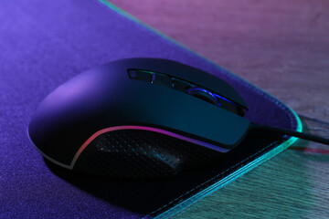 Wall Mural - Black computer mouse and mousepad on wooden table in neon lights, closeup