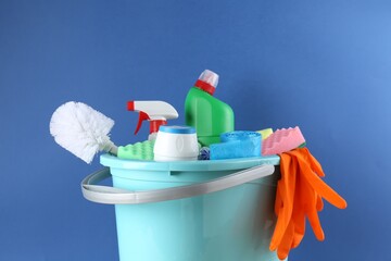 Bucket with different toilet cleaners, sponges, rubber gloves and trash bags on blue background