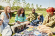 © Seventyfour - Candid shot of four teenagers enjoying picnic on green lawn chatting and laughing while music plays from vintage boombox in park