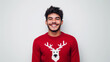 © Favio - Smiling latino young man in a red christmas sweater with reindeer design, he is smiling looking at camera, isolated on white background.