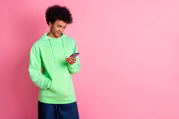 Wall Mural - Portrait of cool young man use smart phone empty space wear green hoodie isolated on pink color background