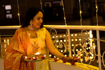 Wall Mural - Diwali Joy: Woman Holding a Plate of Lit Diyas on a Decorated Balcony