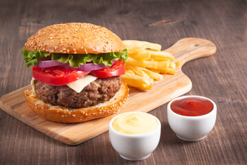 Homemade delicious hamburger with beef, onion, tomato, lettuce and cheese. Fresh burger close up on wooden rustic table with potato fries. Cheeseburger. Burger.