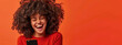 © MD Media - Portrait of smiling african american woman using smartphone isolated on orange background, wearing red sweater with copy space for your text message or promotion banner.
