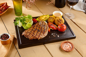 Canvas Print - Delicious Ribeye Steak with Grilled Vegetables on Rustic Wooden Table - Warm and Inviting Atmosphere