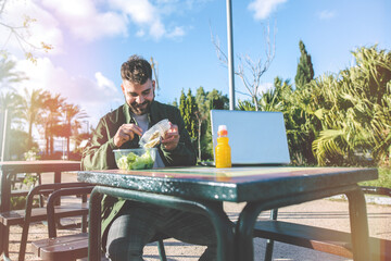 Young man eating a salad while working in a park