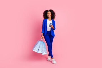 Wall Mural - Full size photo of good mood girl dressed blue jacket holding new outfit in shopping bags smartphone isolated on pink color background