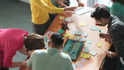 Top view of manager writing idea on sticky notes and explain idea about web design. Professional marketing team or programmer brainstorming idea while looking at tablet with color palette. Symposium.