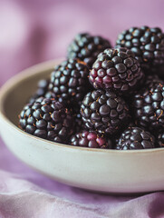 Wall Mural - Closeup of a bowl of fresh blackberries on a purple background