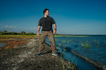 Poster - Young handsome man standing on lake shore on summer day