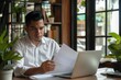 © Nognapas - Young busy latin professional business man checking document working at laptop computer in office. Serious businessman accountant expert reading legal paper company file overview at workplace.