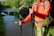 © pressmaster - Hands of unrecognizable female backpacker holding trekking sticks while standing in front of camera or walking along riverside