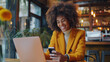 © tiagozr - Cheerful Black woman using laptop and smartphone in a stylish urban café.