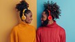 © ProPhotos - Young African American couple with headphones exchanging warm smiles against yellow and blue background, reflecting a romantic and joyful interaction.