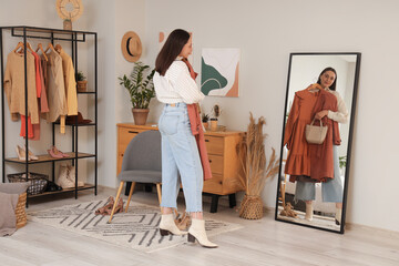 Sticker - Young woman trying on stylish clothes with bag near mirror at home