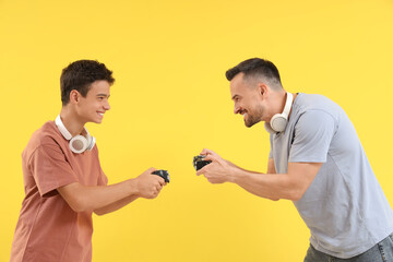 Canvas Print - Teenage boy with his father playing video game on yellow background