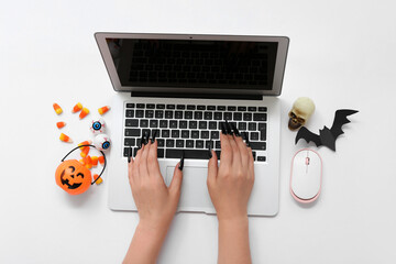 Canvas Print - Female hand with modern laptop and Halloween decorations on white background