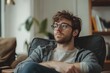 © Minerva Studio - Pensive young man wearing glasses is sitting and relaxing at home