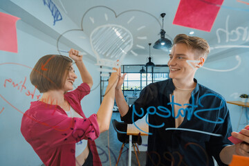 Two smart cooperative business people giving a high five to celebrate the successful start up project while brainstorming marketing idea in front of glass board by using mind map. Immaculate.