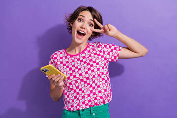 Sticker - Photo of overjoyed glad cheerful girl wear trendy clothes hand touch face v-sign good mood cool party isolated on purple color background