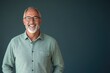 © kitipol - Senior male presenter in a casual shirt, smiling, standing against a solid blue-gray background with space for text
