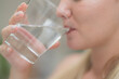 © ultramansk - A beautiful European woman smiles happily, holding a glass of water, drinking natural mineral water from a clear glass, inside a residential. A healthy woman shows her face, complete physical health.