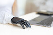 © ultramansk - A young woman is using a robotic prosthetic arm hand attached to her body to work on a desk. she is doing computer document and communication work. woman tries to control the smart arm in her home.
