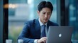 © Generative AI - Young adult serious busy Asian business man manager wearing suit typing on laptop using computer working on digital project financial market data software management sitting at desk in : Generative AI