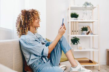 Wall Mural - Relaxed Woman Sitting on a Cozy Sofa, Holding Mobile Phone and Smiling while Enjoying Online Games and Reading.