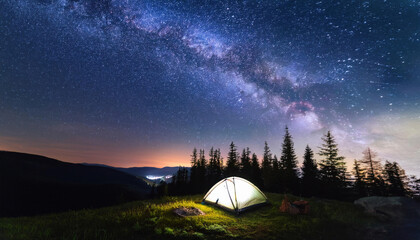a tent with light in forest on mountain at night with starry milky way galaxy in the sky for outdoor