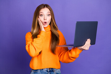 Poster - Portrait of youth blonde hair cute happy smile girl in orange sweater studying online using laptop touch cheek isolated on violet color background