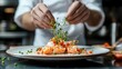 © Phirakhup - A chef elegantly garnishes a gourmet shrimp dish with fresh herbs, showcasing culinary skill and creativity in a beautiful kitchen setting.