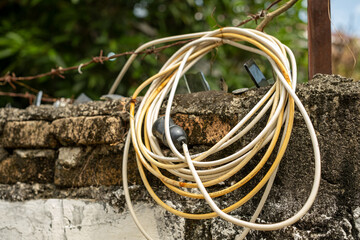 Old electrical cable is hanging on a stone wall with barbed wire on top, showing a lack of safety and security