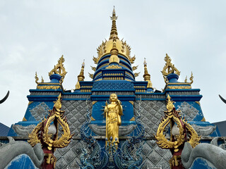 Wall Mural - Blue temple at Chiang Rai, Thailand, or Wat Rong Suea Ten in Thai. This temple hosts many Buddhist ornaments painted in all blue and gold colors. Behind the temple is Buddhist pagoda stupa in gold.