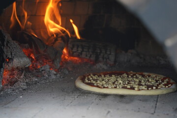 Pizza is baked in a stone oven with coals outside.