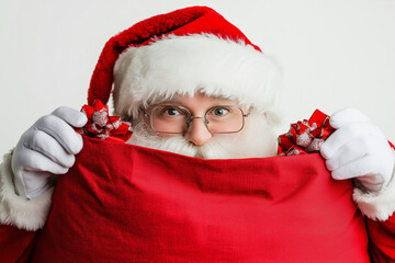 Wall Mural - santa with a red hat and glasses holding a red bag. He is hiding something in the bag