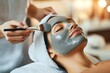 © dreamdes - Young woman receiving clay facial mask in spa salon. Beauty treatment and skincare procedure concept. Wellness and relaxation. Banner, advertisement. Close-up portrait