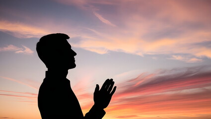 Silhouette of a young man in a praying pose. Set against a vibrant sunset sunrise sky